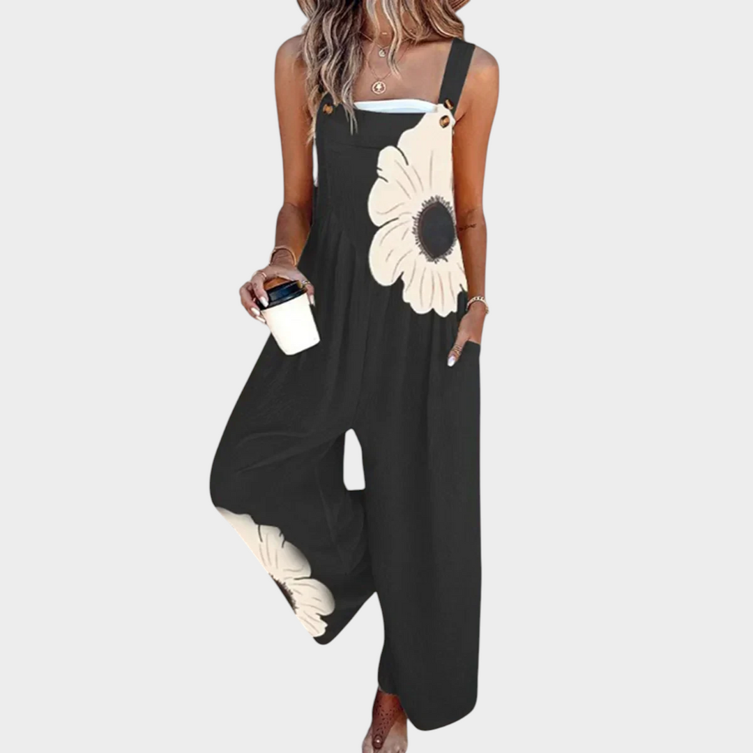 Aurore Paris bohemian jumpsuit in black with large white floral print, featuring wide legs and adjustable straps.