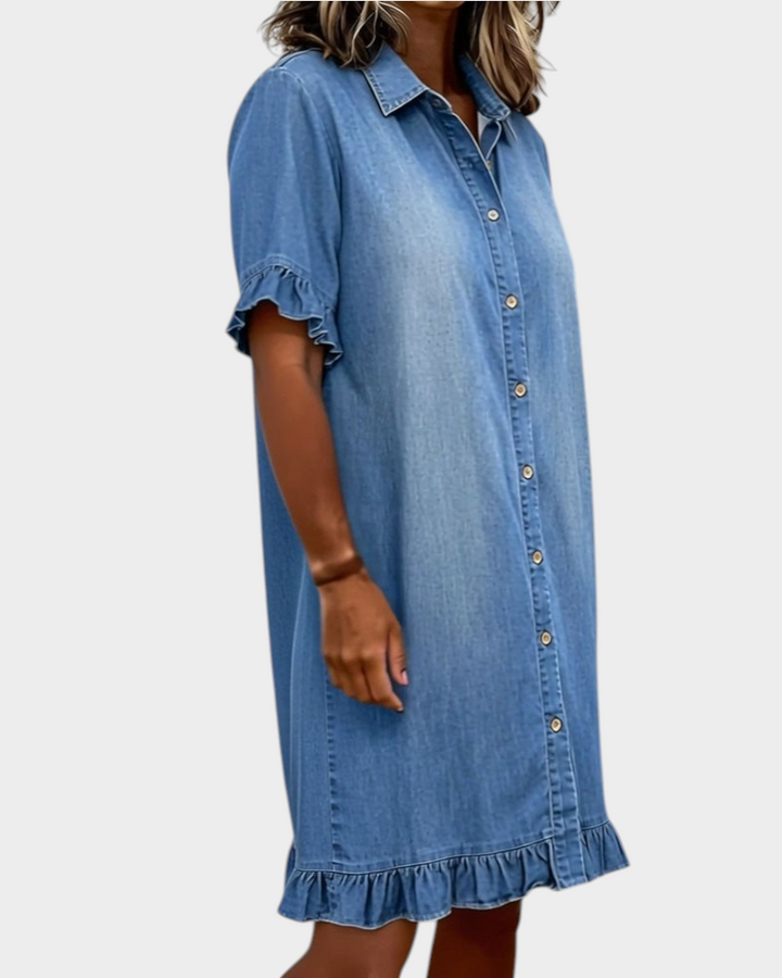 Aurore Paris blue denim shirt dress with a collar, button front, and ruffled sleeves and hem, worn by a woman.